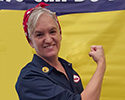 A woman impersonating Rosie the Riveter smiles and flexes her bicep