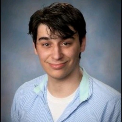 Headshot of a young man with dark hair and a slight smile, wearing a blue and white striped button-down shirt over a white undershirt against a blurred blue background.